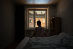 Persona sentada en su cama, intentando dormir, no lo consigue debido al insomnio