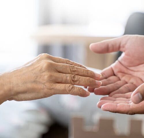 Manos de cuidador extendida hacia la mano de un anciano