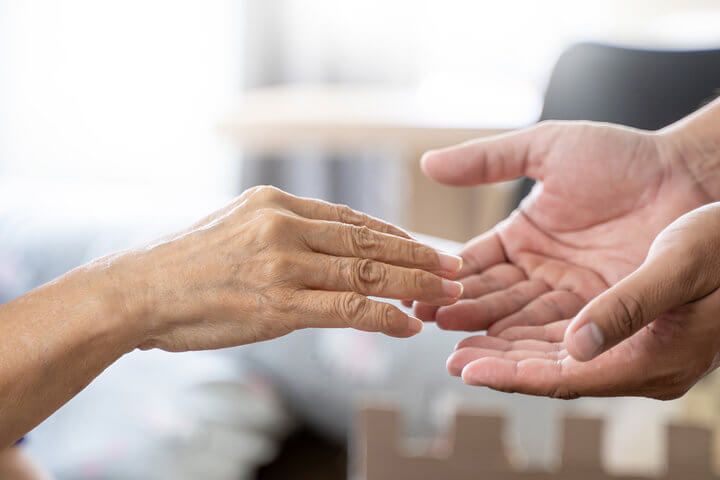 Manos de cuidador extendida hacia la mano de un anciano